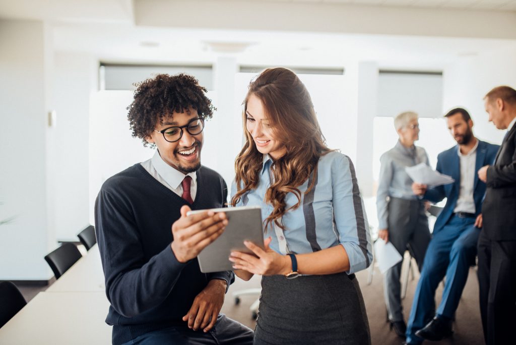 Happy young coworkers looking at digital tablet while standing at office